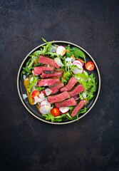 Modern style traditional fried dry aged bison beef rump steak slices with vegetable, lettuce and mustard dressing served as top view on a Nordic design plate with copy space