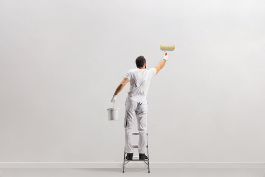 Rear view shot of a painter holding a bucket and painting a wall on a leader