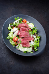 Modern style traditional fried dry aged bison beef rump steak slices with vegetable, lettuce and parmesan cheese served as top view on a design plate with copy space
