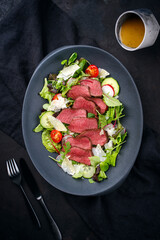 Modern style traditional fried dry aged bison beef rump steak slices with vegetable, lettuce and mustard dressing served as top view on a Nordic design plate with copy space