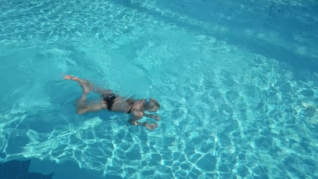 Active young woman diving in pool and splashing water. Lady relaxing on tropical resort.