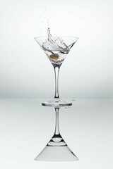 A cocktail glass with martini splash and an olive.