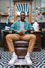 Portrait of young African man sitting on chair in barber shop.