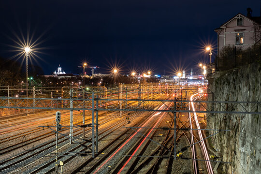 Bypassing trains cast light trails on the rail tracks with a beautiful city skyline in the background.