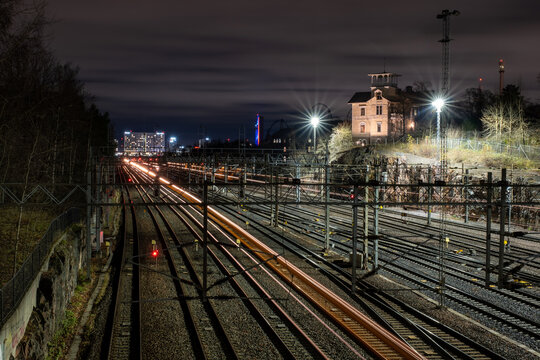 Bypassing trains casting light trails on the railtracks with beautiful city skyline on the background.