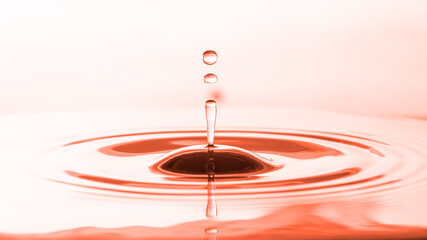Abstract droplets of water on water surface to create ripples with orange-pink background.