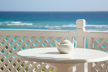 White teapot on a white table against a blue sea background. Selective focus on teapot - 469021731