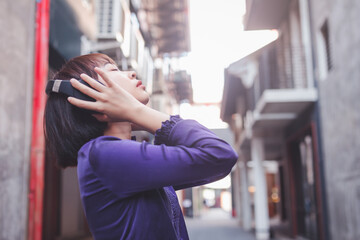 Happy young asian woman listening to music with headphones on the street.