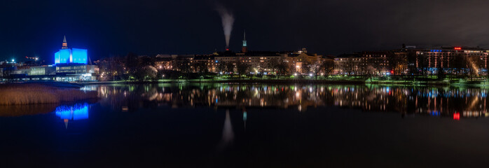 Fototapeta premium Beautiful city skyline casting reflections on the calm water during the night.