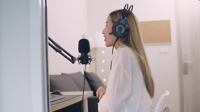 Beautiful Young Asian woman podcaster recording podcast and live streaming content for social media at home studio.