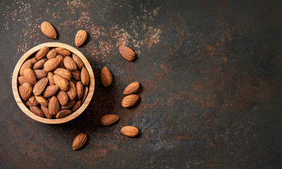 Almond top view on dark old vintage style table background. Almonds in a wooden bowl and nuts lay freely. Healthy food and snacks Organic vegetarian food. Top view.