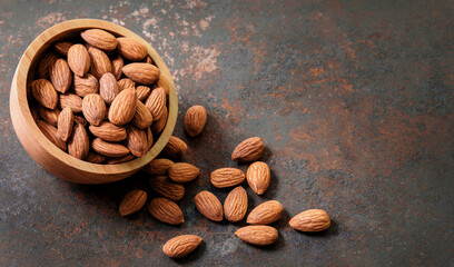 Almond top view on dark old vintage style table background. Almonds in a wooden bowl and nuts lay freely. Healthy food and snacks Organic vegetarian food. Top view.