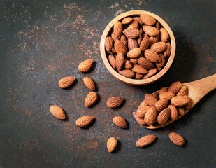 Almond top view on old dark vintage style background. Almonds in a wooden bowl and a wooden spoon and nuts are laid freely. Healthy food and snacks organic vegetarian food.