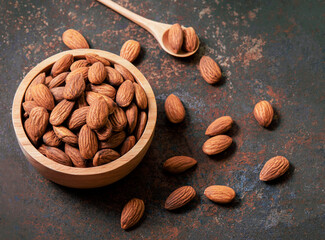 Almond top view on old dark vintage style background. Almonds in a wooden bowl and a wooden spoon and nuts are laid freely. Healthy food and snacks organic vegetarian food.