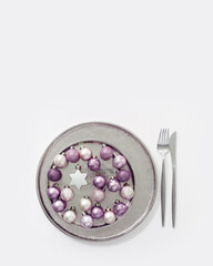 Christmas table setting concept with sparkling small balls lavender color and bauble star in metal plate or tray, knife, fork. New Year winter holiday abstract food, trend color