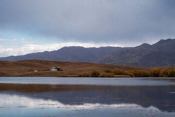 Old home near lake with mountains and clouds reflections on water.