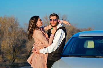 Young loving couple hugs outdoors near car. Sunny autumn day. Lifestyle, youth and adventure concept. Freeluft aesthetics. Casual style.