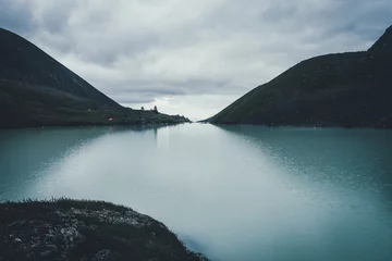 Cercles muraux Violet pâle Dark atmospheric landscape with orange tent near mountain lake in highland valley under cloudy sky in dark time. Ripples on mountain lake water in dusk. Dark scenery with water ripple on highland lake