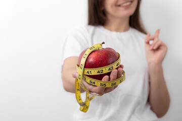 Fresh red apple with a measuring tape in female hands, close-up.