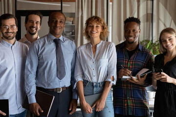Group portrait of smiling young mixed race business people employees managers posing together in modern office room. Joyful multiracial diverse teammates looking at camera, professional career concept