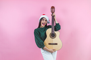 Portrait of young latin woman holding guitar music with copy space in a christmas concept on pink...