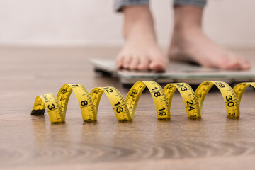 Female leg stepping on weigh scales with measuring tape.