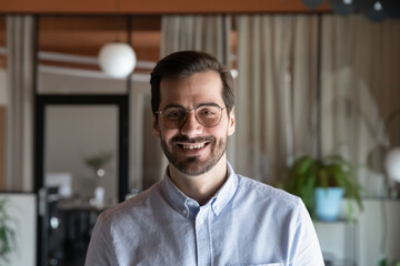 Obraz premium Head shot smiling confident young ceo executive male manager employee worker businessman in eyewear posing in modern office room, professional profile photo, video call virtual meeting concept.