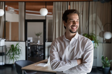 Happy motivated young hispanic businessman manager employee standing with folded arms in modern...