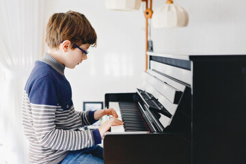 School boy with glasses playing piano in living room. Child having fun with learning to play music...