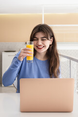 Attractive young woman with a glass of juice sits in front of a laptop.