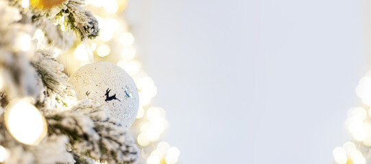 Decorated Christmas tree with white ball with deer. Banner. A branch of a snow-covered tree with Christmas decor with a soft focus. Copy space. Place for text
