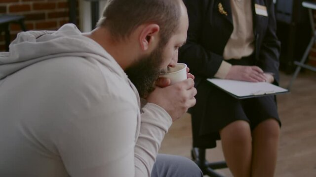 Close up of man trembling while drinking cup of coffee at aa group meeting with therapist. Desperate person with shaky hands attending group therapy session to receive help and support.