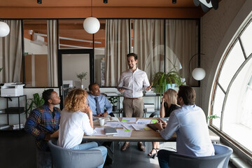 Happy young hispanic male ceo executive manager boss leading brainstorming meeting with multiethnic colleagues, discussing project details or briefing problem solution in modern office room.