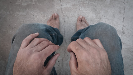 Dirty and bare feet on concrete. Hands. A homeless and wandering person. The concept of poverty. Stress and depression. A hopeless situation.