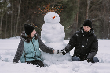 Couple of teenagers building snowman together in winter