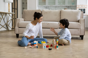 Loving young Indian mother and little son playing together on heating floor, building towers from toy construction bricks, talking, enjoying leisure, playtime, creative game. Motherhood concept