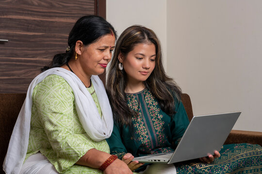 Indian mother and daughter watching into the laptop at home. Modern daughter helping her mother with technology. Mother and daughter at home.