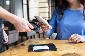 Paypass, male hands holding black pos terminal and female brings smartphone. - obrazy, fototapety, plakaty