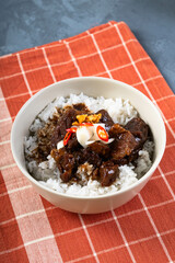 a rice bowl of chinese braised beef shank topped with red onion and chili pepper