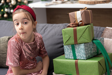 A little girl enjoys a lot of Christmas gifts sitting on the couch at home.