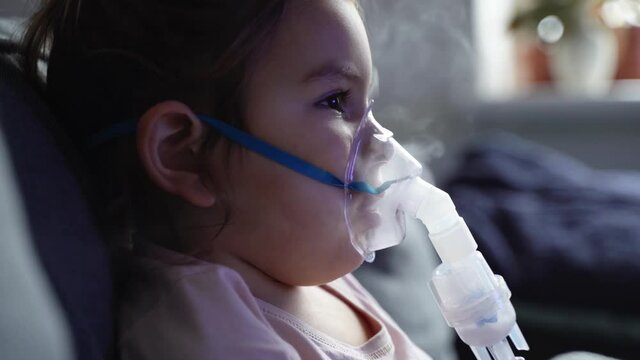 Sick adorable preschool girl with nebuliser mask at home. Treatment for bronchitis with inhaling medicine nebula.