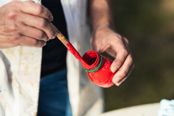 Artisan holding a brush and a pot with red paint outdoors