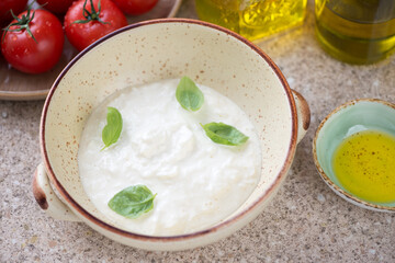 Bowl of stracciatella or cheese produced from italian buffalo milk, studio shot on a beige marble background, middle close-up