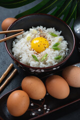 Black bowl with japanese tamago kake gohan, vertical shot on a black stone surface, middle close-up