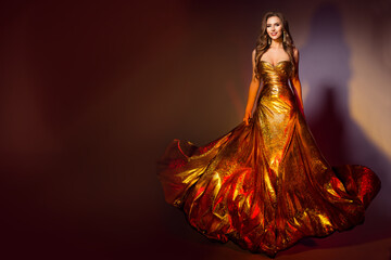 Fashion Model in Long Golden Dress. Smiling Beauty Woman in Evening Shining Fluttering Gold Gown...