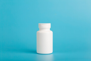 Jar of pills isolate. White plastic jar for medical pills, drugs and vitamins on a blank blue background.