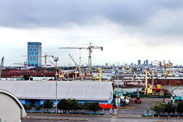 Fototapeta premium Cargo terminal for unloading steel plates from bulk carrier by ships cranes. View of the pier, cranes and various equipment. Port of Surabaya. Indonesia, January, 2021.