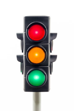 Vertical view of a traffic light showing illuminated red, amber, and green lights.  Concept image illustrating control of the COVID pandemic and confusion.


