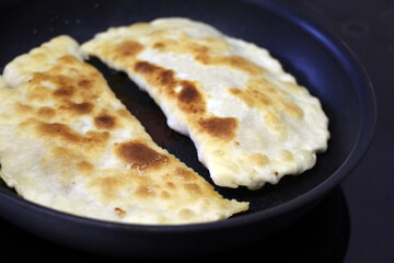 Frying chebureks on electric induction stove, traditional eastern dish. Homemade tortillas with meat on black pan fried in oil