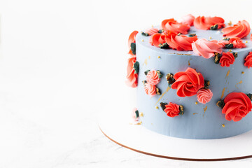 Birthday cake with blue cream cheese frosting decorated with red flowers on the white background